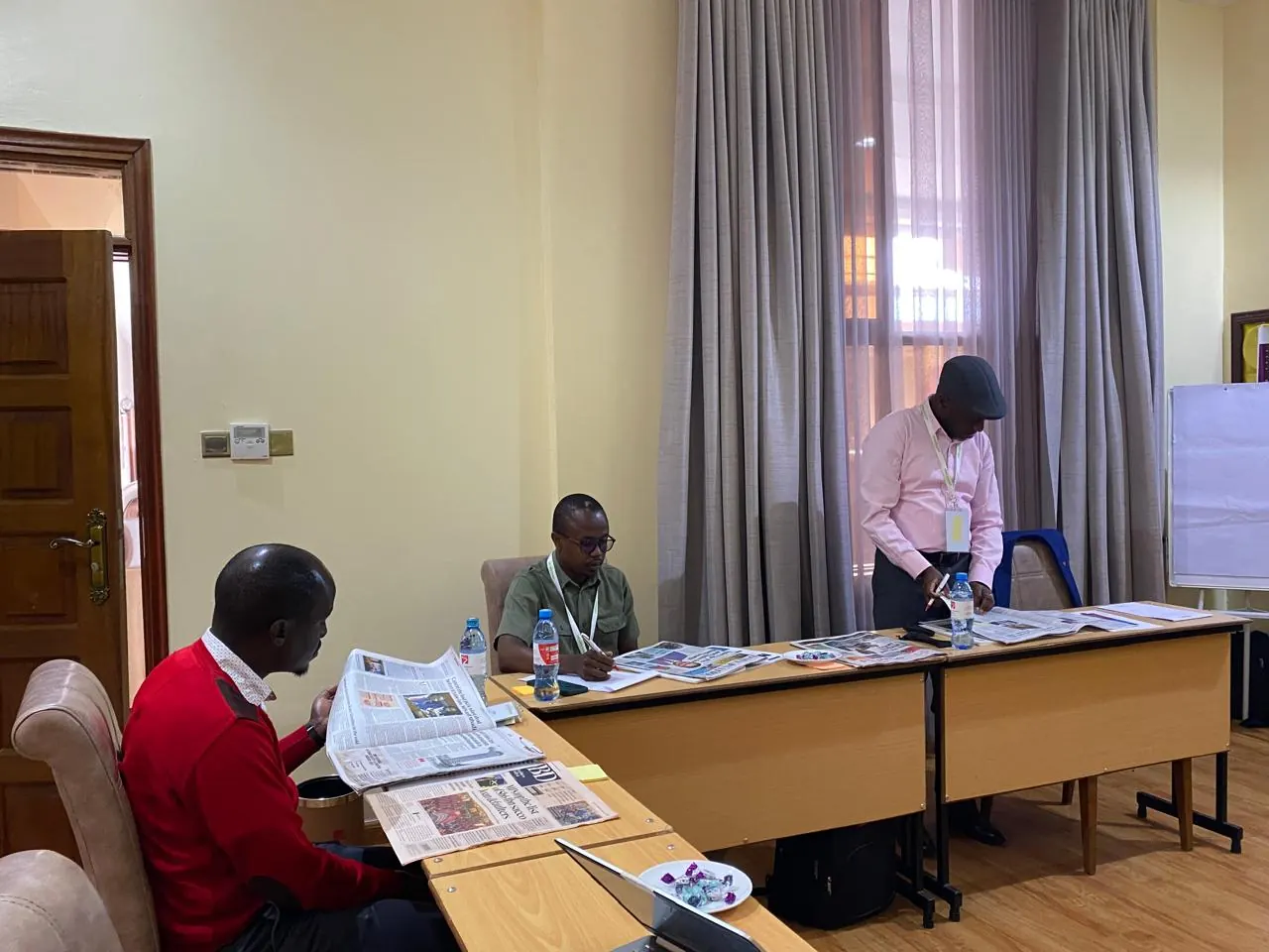 Delegates at a table in a training room; one stands to write.