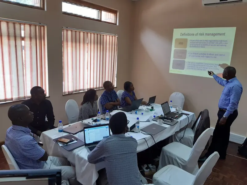 A facilitator points to a projected slide while participants with laptops look on.